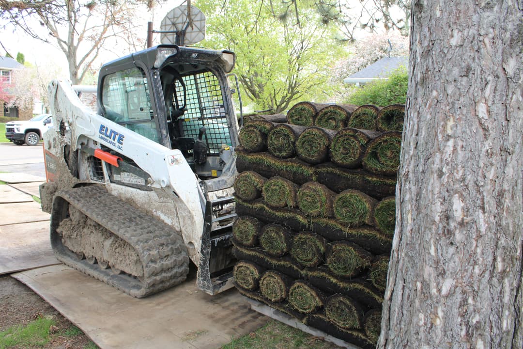 Bobcat skid steer loader next to stacked rolls of sod on a construction site.