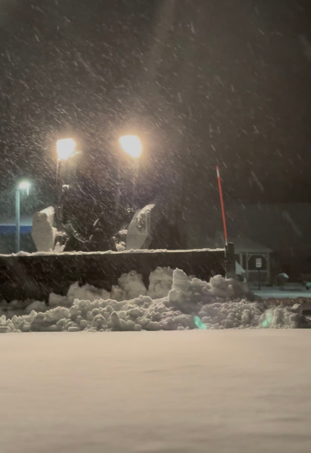 Snowy night scene with falling snow and illuminated streetlights reflecting off the ground.