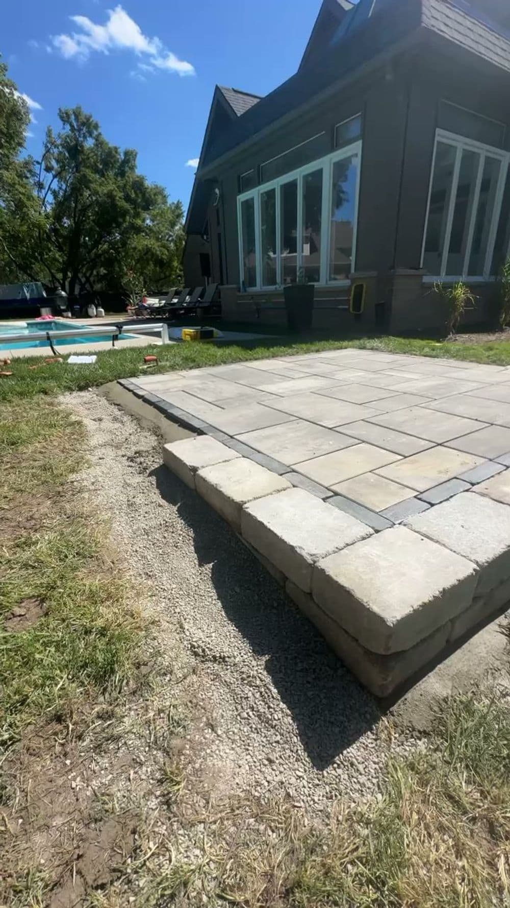 Patio installation featuring paver stones, lawn, and a house with large windows.