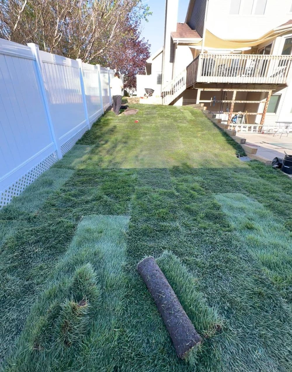 Lush green lawn installation in a backyard with freshly rolled sod and a wooden deck.
