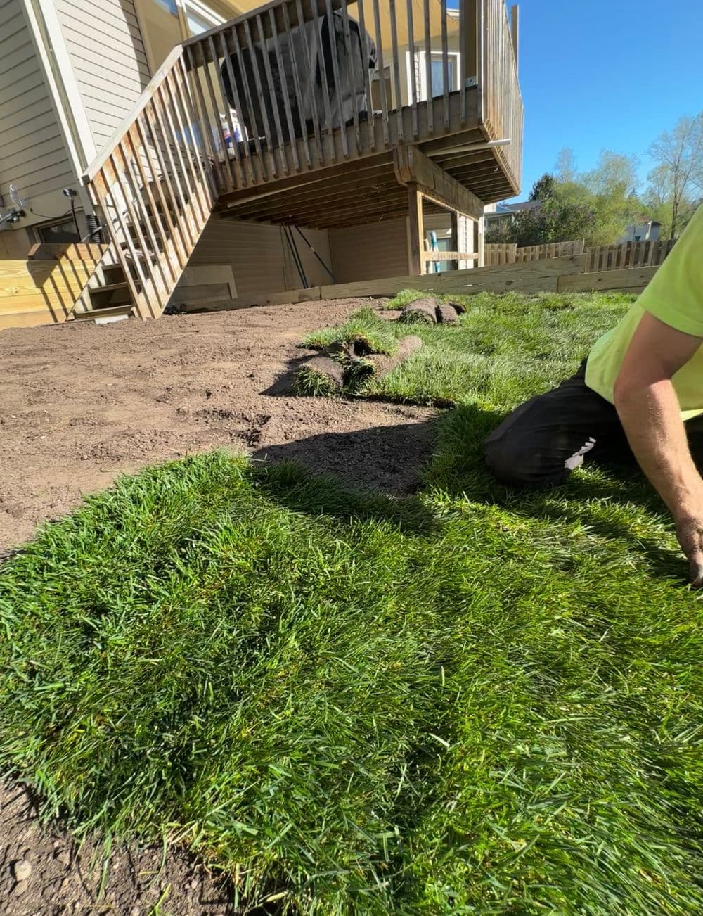 Laying fresh sod in a backyard near a deck on a sunny day.