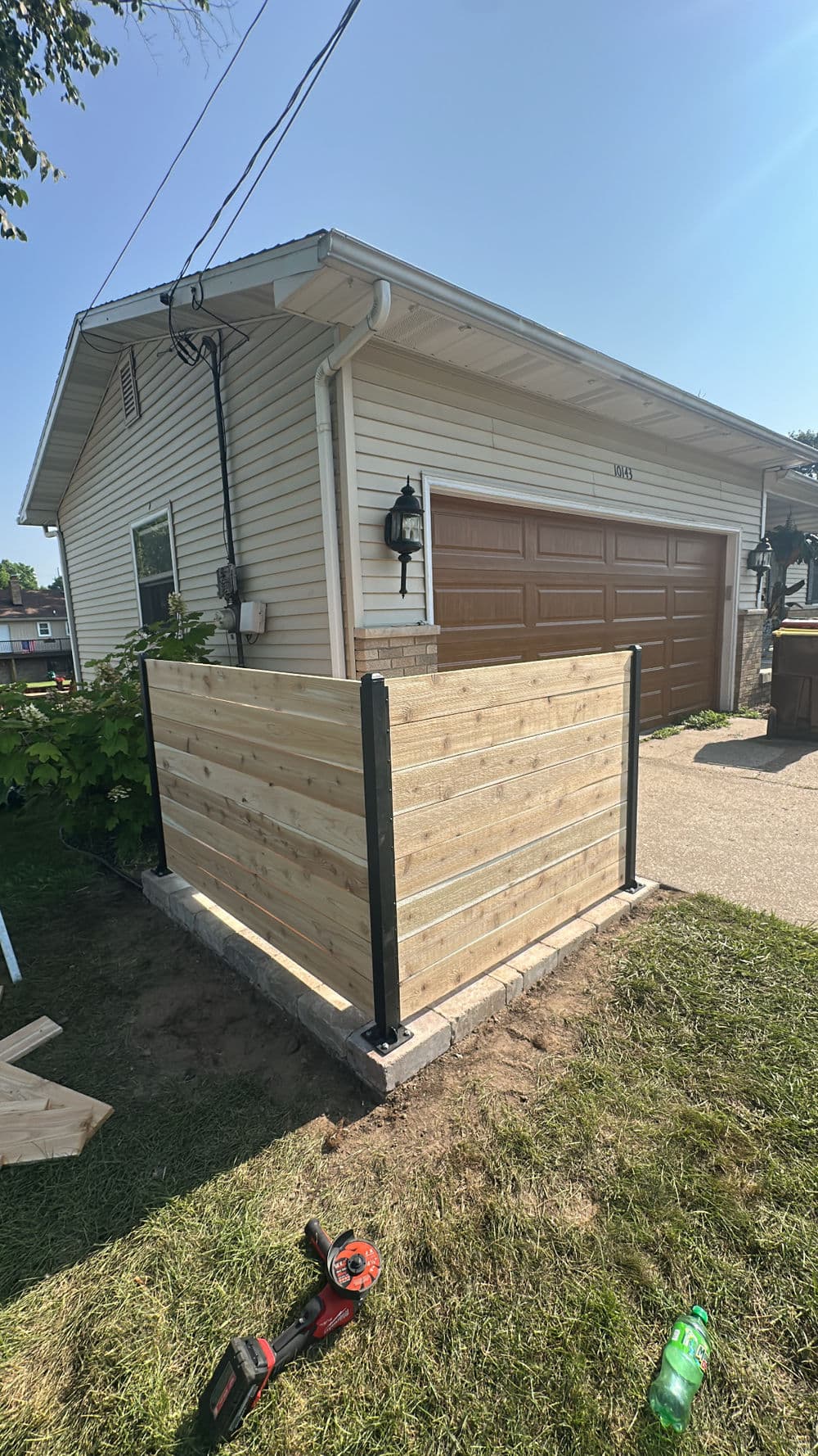Wooden fence enclosure with black metal posts beside a garage on a sunny day.