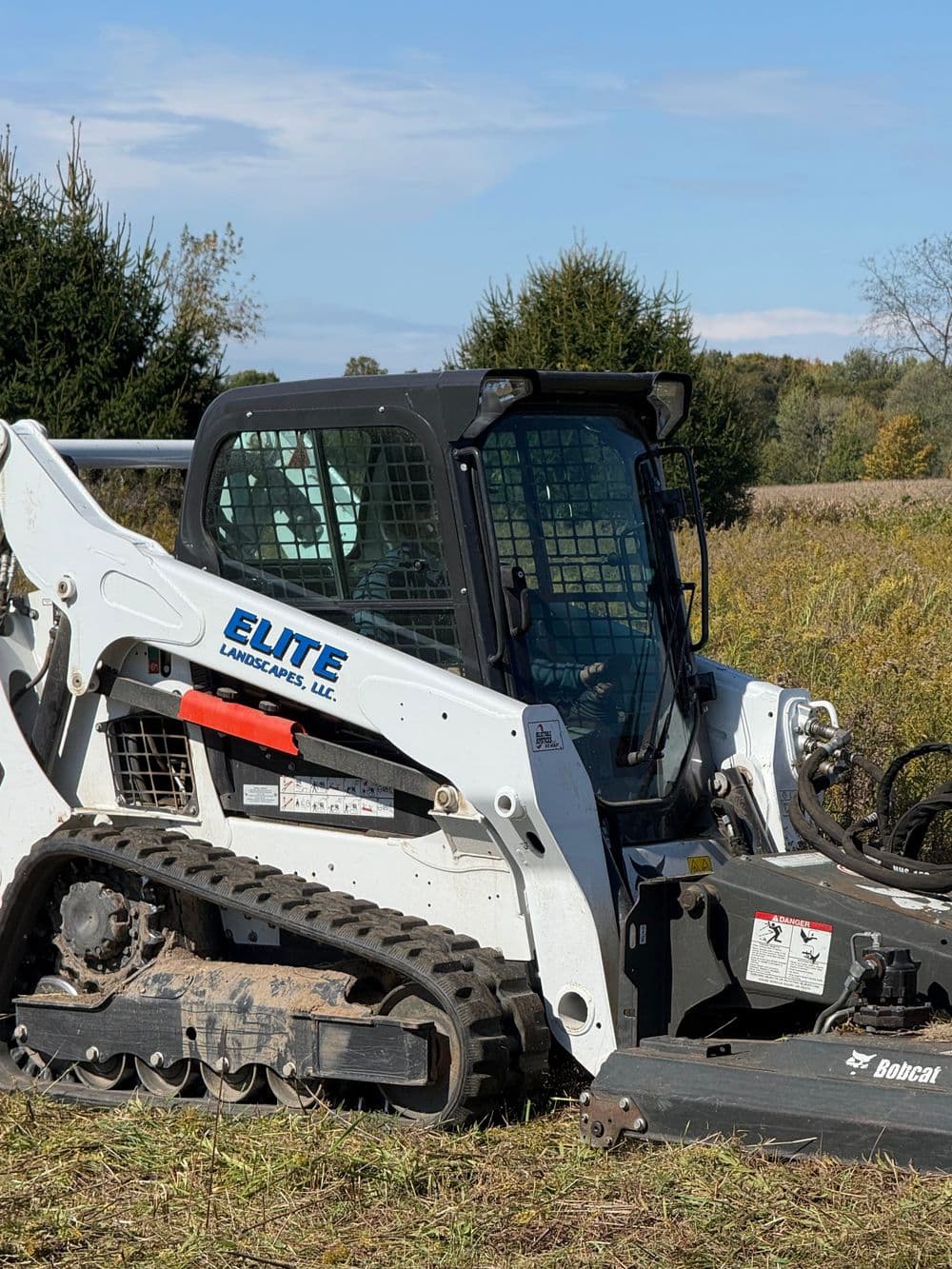 Bobcat skid steer loader from Elite Landscapes, LLC in a rural landscape setting.
