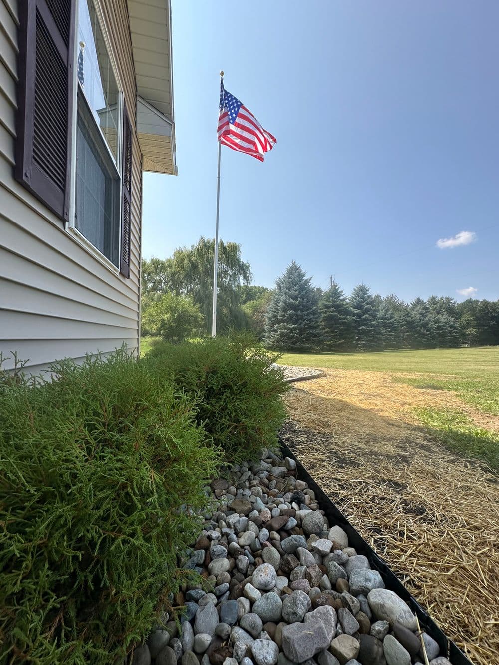 American flag flying beside a house, with landscaped rocks and greenery in the foreground.