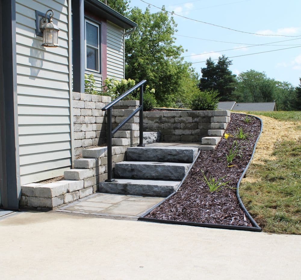 Stone steps leading to a house, surrounded by mulch and landscaping features.