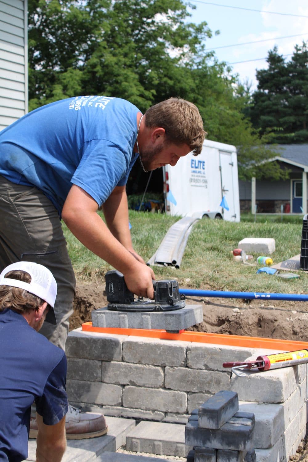 Construction worker using a power tool on a stone structure with a helper nearby.