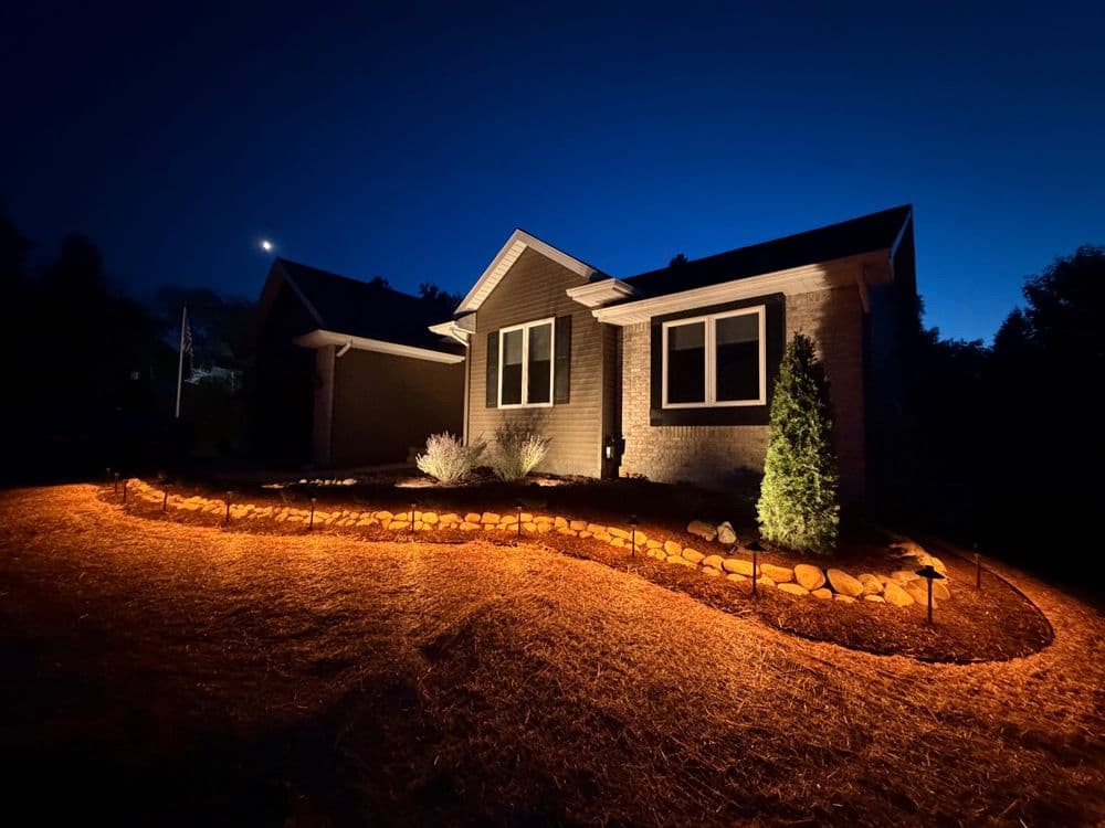 Beautifully lit home exterior at night with soft landscape lighting and a cozy atmosphere.