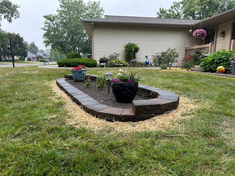 Flower bed renovation with colorful plants, stone border, and lush green lawn in suburban setting.