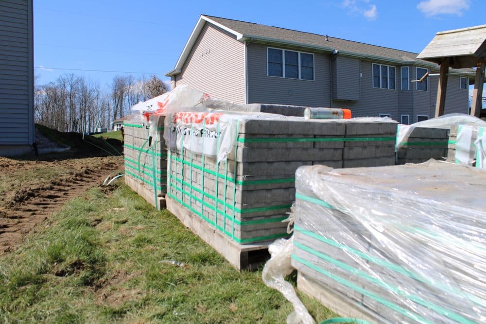 Stacks of wrapped concrete slabs on a construction site next to residential buildings.