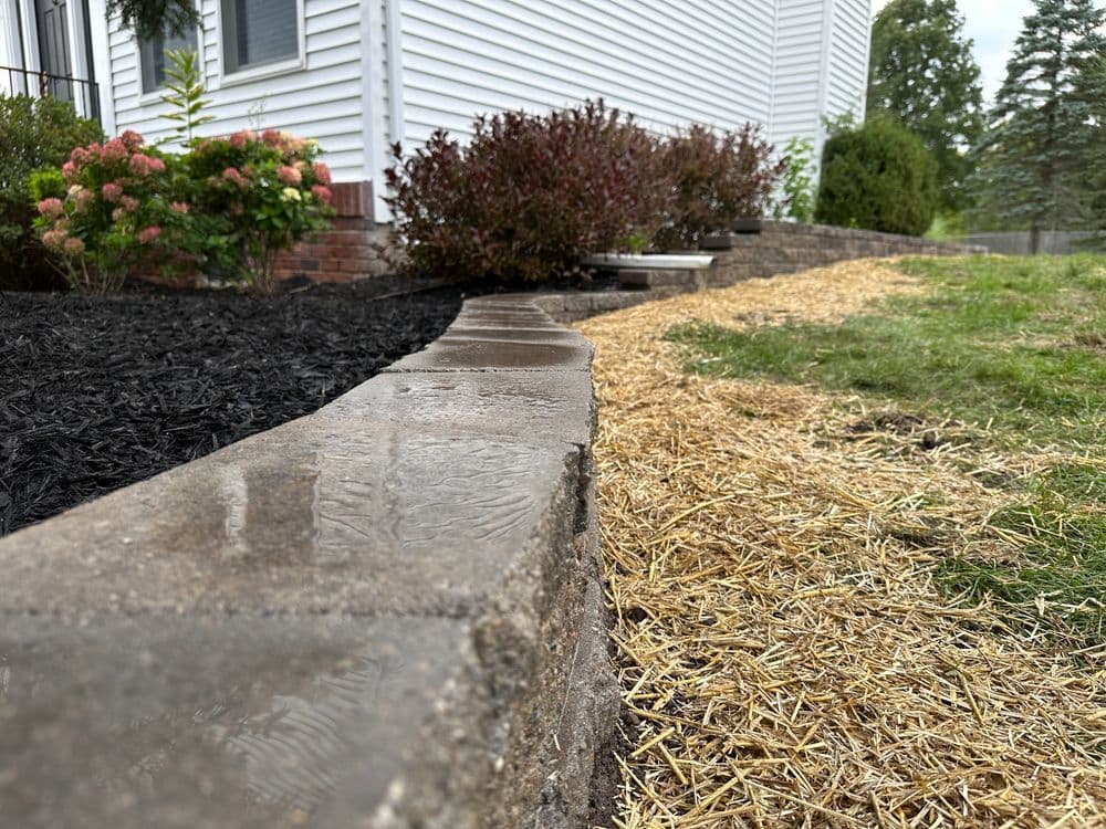 Landscape border with wet stone, contrasting mulch, and recent straw application near house.