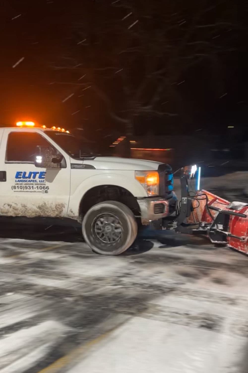 Elite Landscaping snow plow truck clearing snow in a winter setting at night.