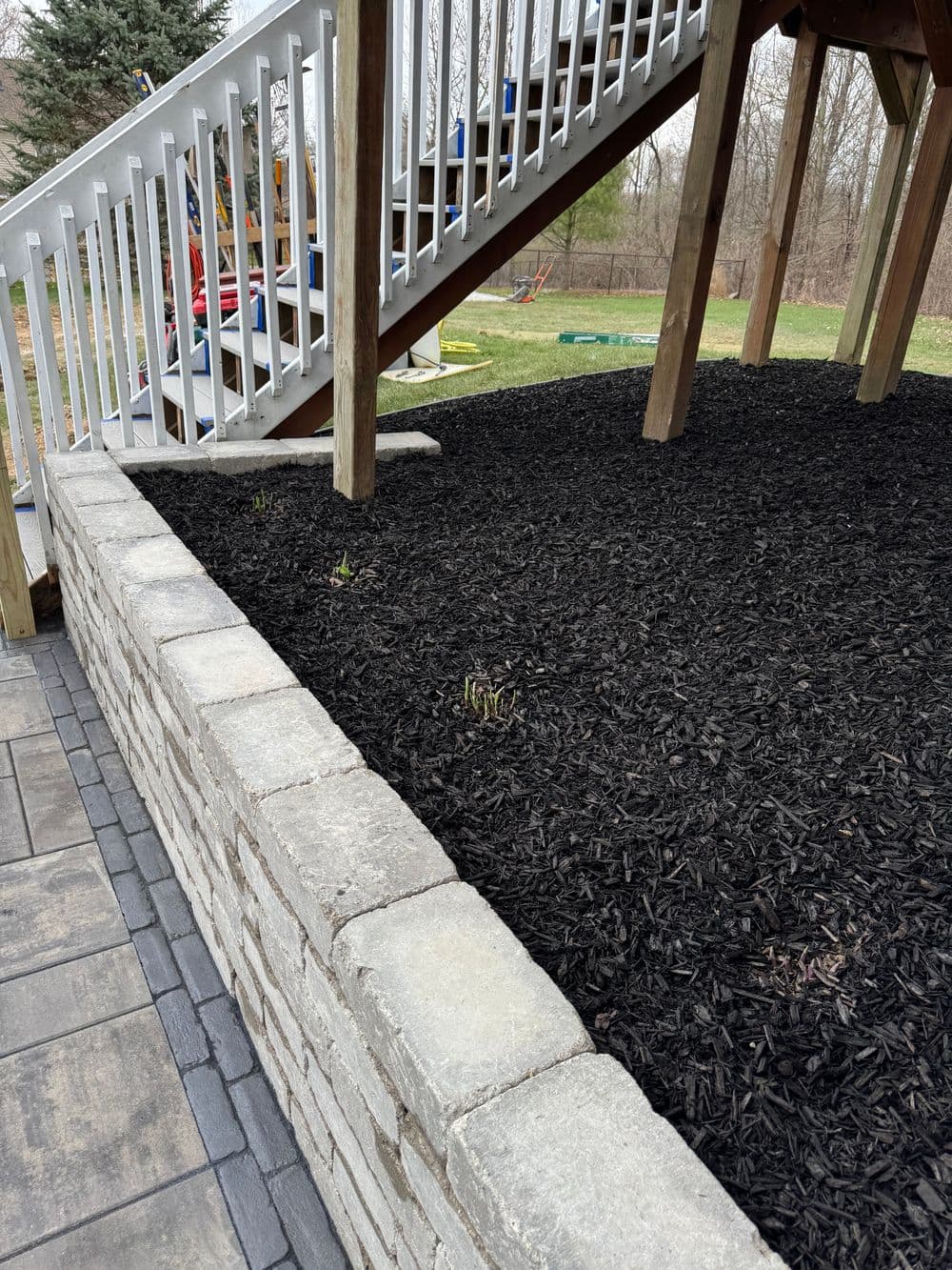 Black mulch landscaping near a wooden stairway with green grass and playground in the background.