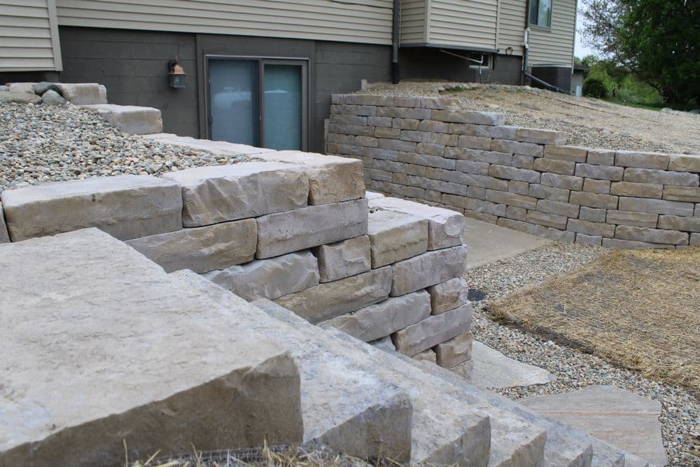 Stone retaining wall with gravel pathway beside a residential building in outdoor setting.
