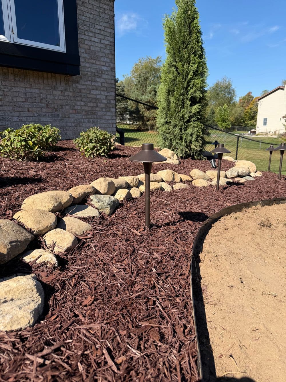 Landscape with decorative stone border, mulch, and solar garden lights in a yard setting.