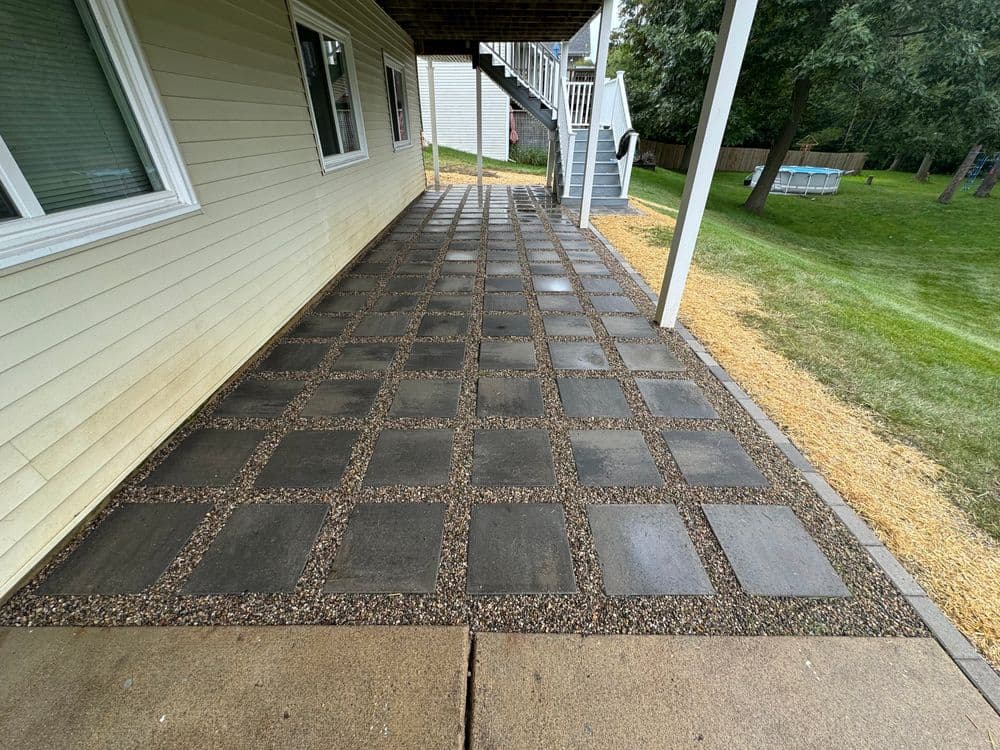Patio with rectangular stone pavers and gravel, featuring grassy area and house exterior.