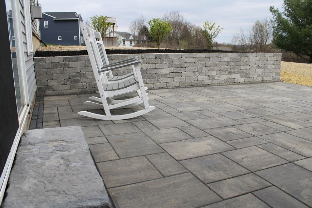 Rocking chairs on a stone patio with a landscaped wall and scenic backdrop.