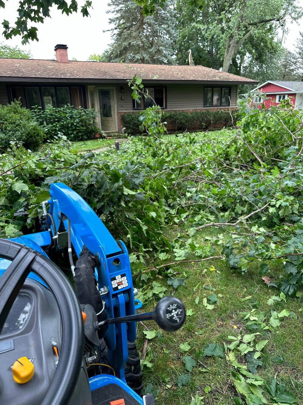 Tractor clearing tree branches from yard near a suburban house.