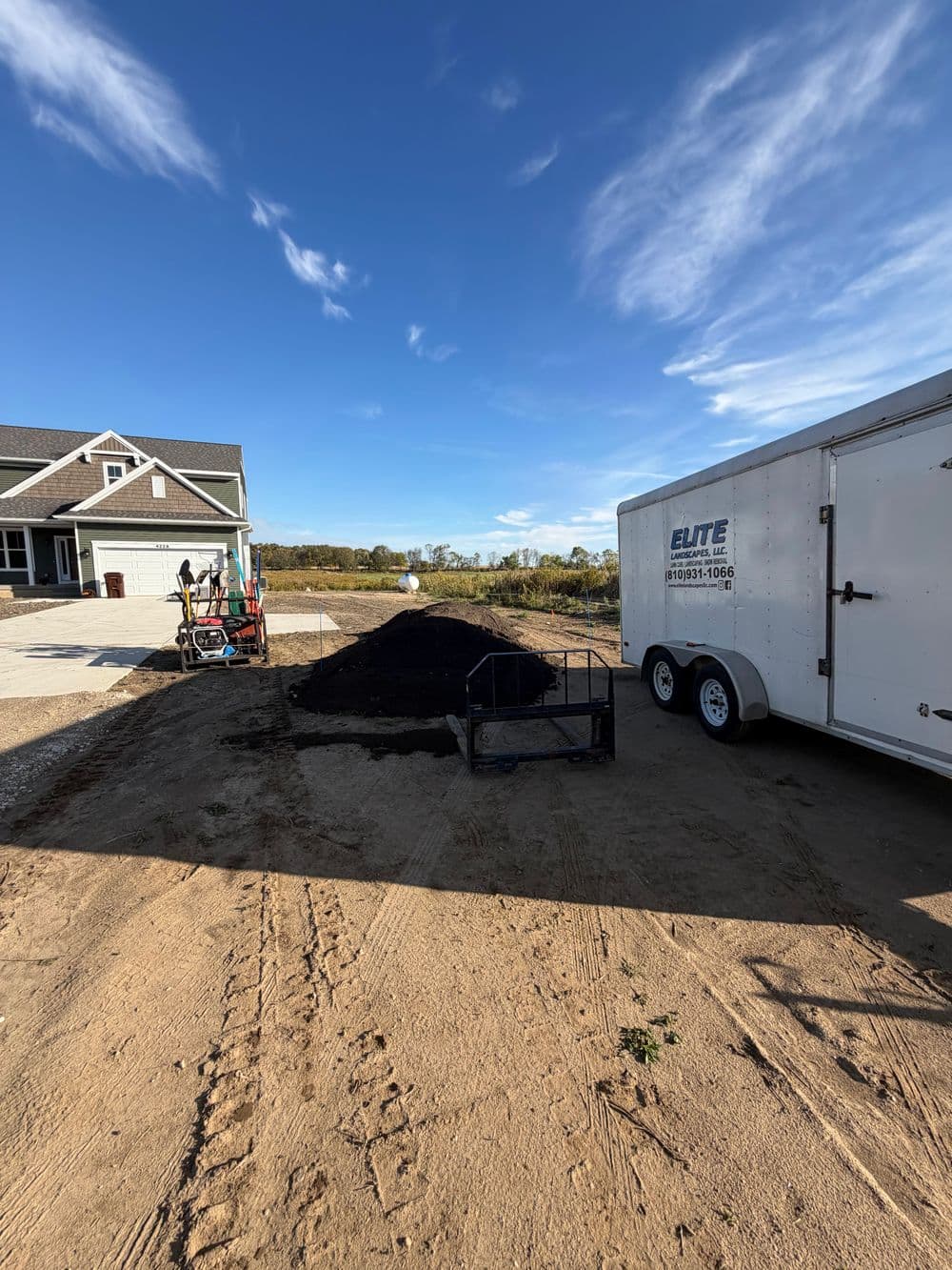 Workers preparing landscaping with mulch near a trailer and new construction home.