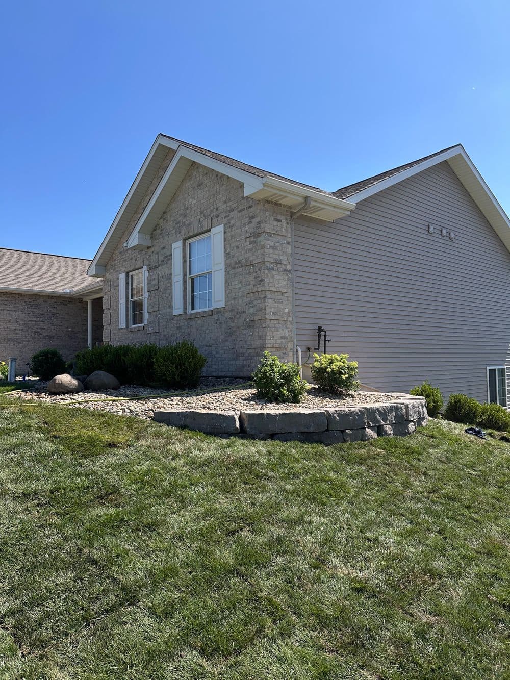 Modern single-story home with stone facade and landscaped yard under clear blue sky.