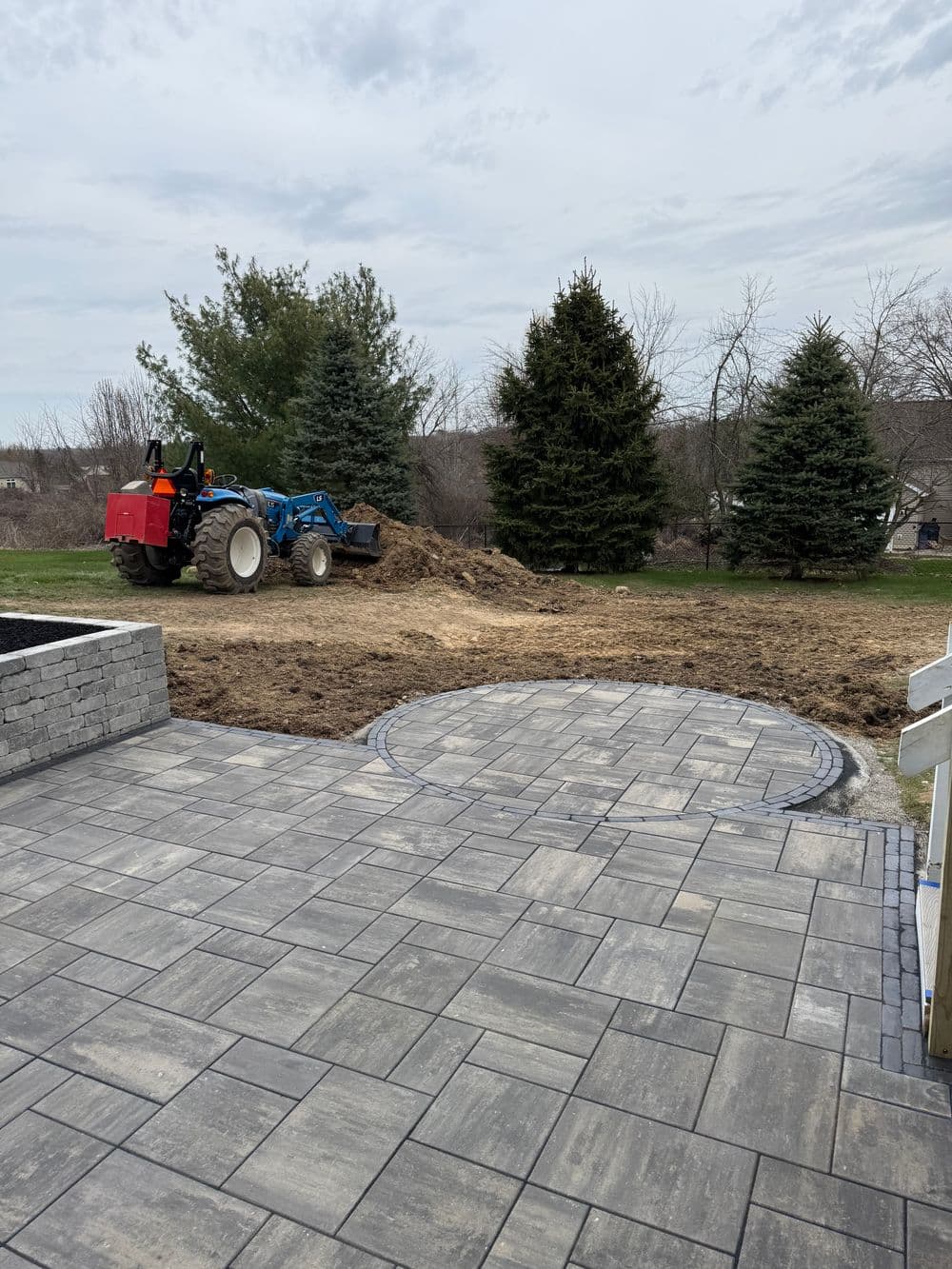Tractor clearing land for landscaping project with circular stone area in foreground.