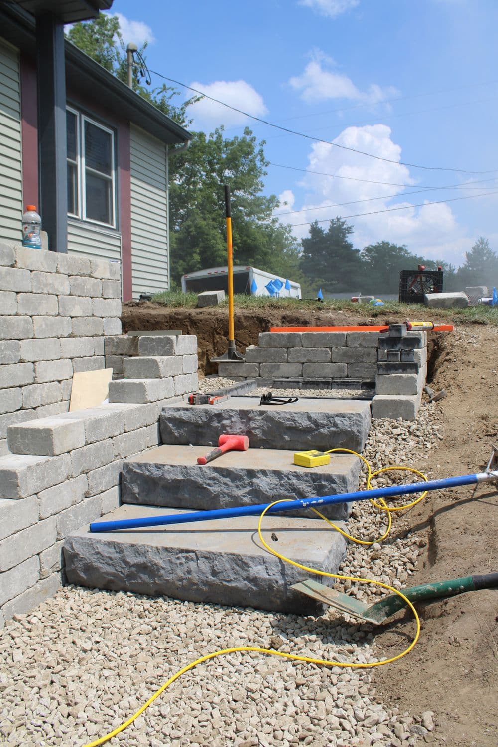 Stone steps leading to a house, surrounded by construction tools and gravel.