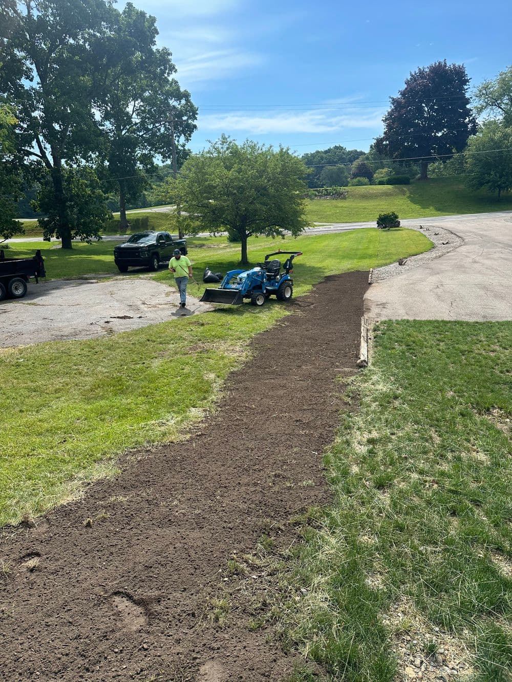 Landscape worker using a tractor to shape a new path in a green park area.