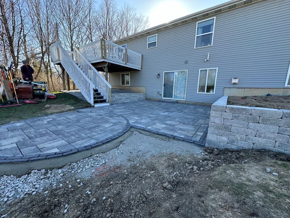 Patio area with pavers and steps leading to a home, surrounded by landscaping and gravel.