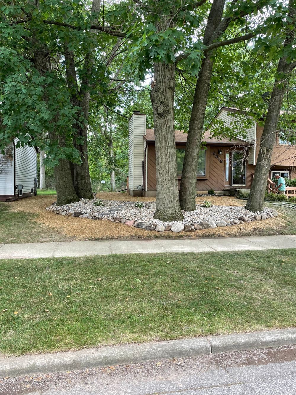 Front yard landscaping with stone border and trees around a contemporary house.