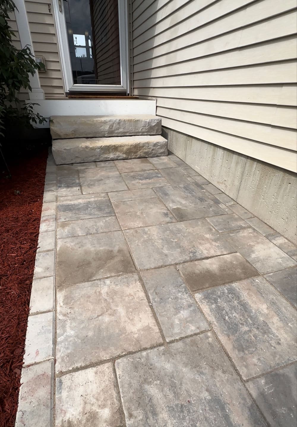 Paved walkway leading to a home entrance with stone steps and red mulch landscaping.