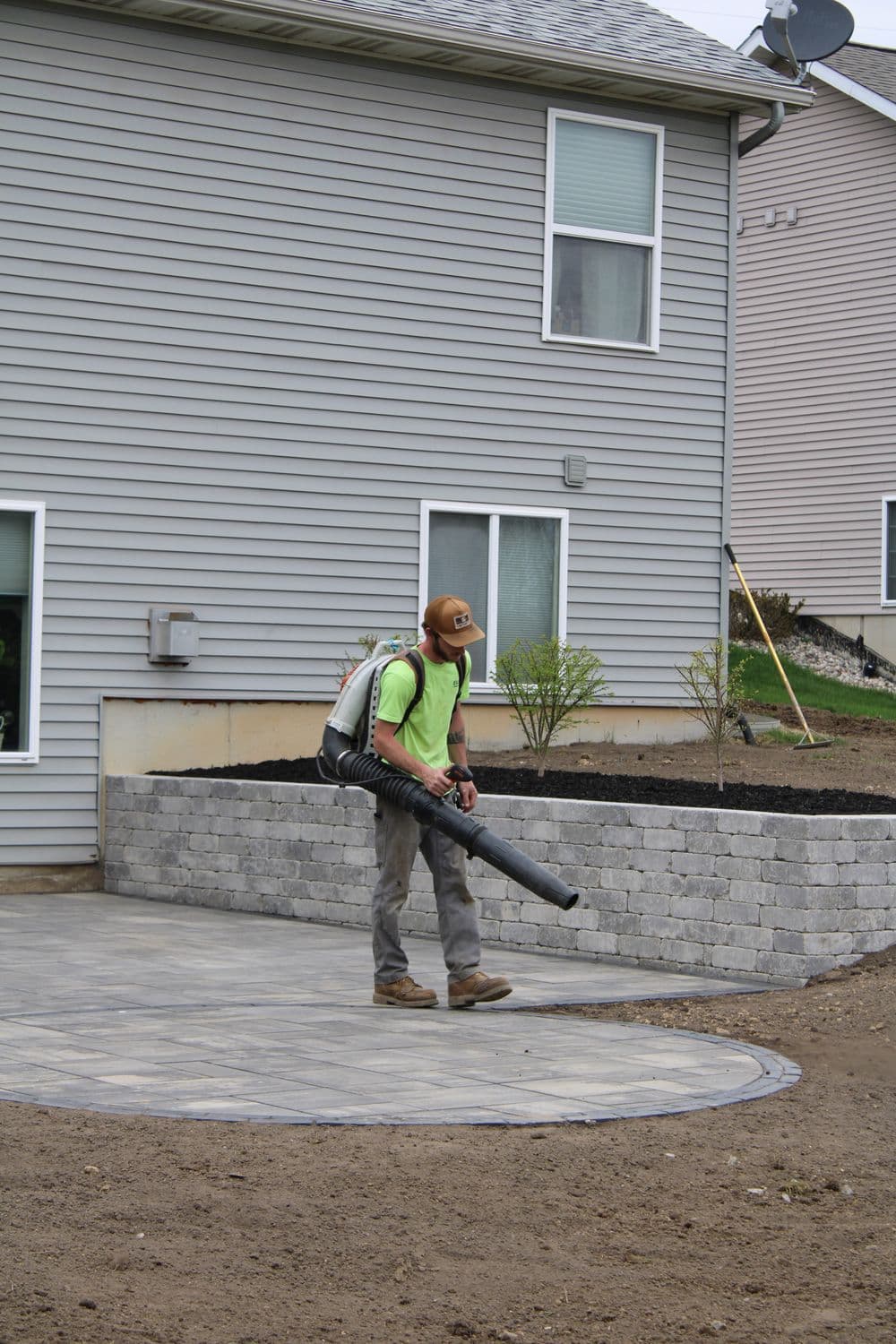 Landscaper using a leaf blower on a patio in a residential backyard.