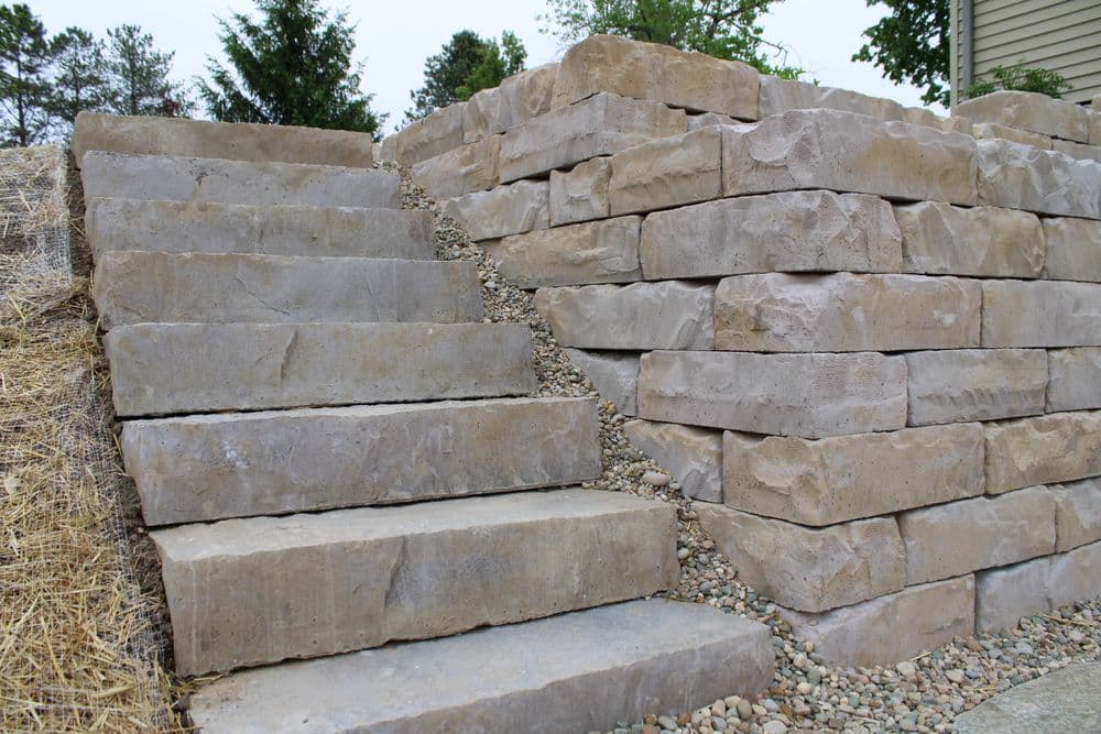 Stone steps leading to a landscaped area with a retaining wall made of large stones.