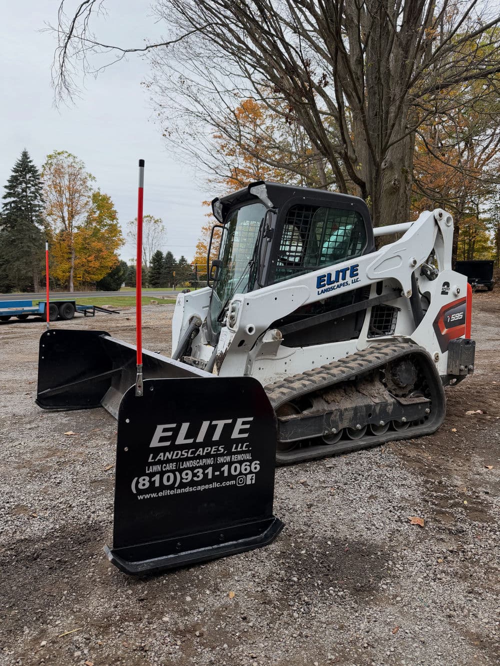 Bobcat skid steer loader with snowplow attachment, parked at a landscaping site. Elite Landscapes logo visible.