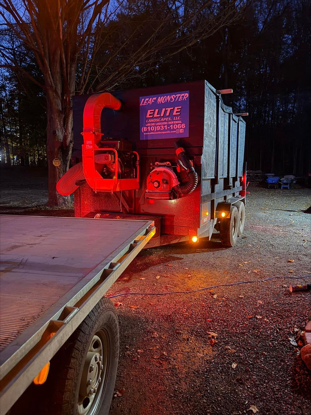 Leaf Monster Elite trailer with leaf vacuum equipment in a wooded area at dusk.