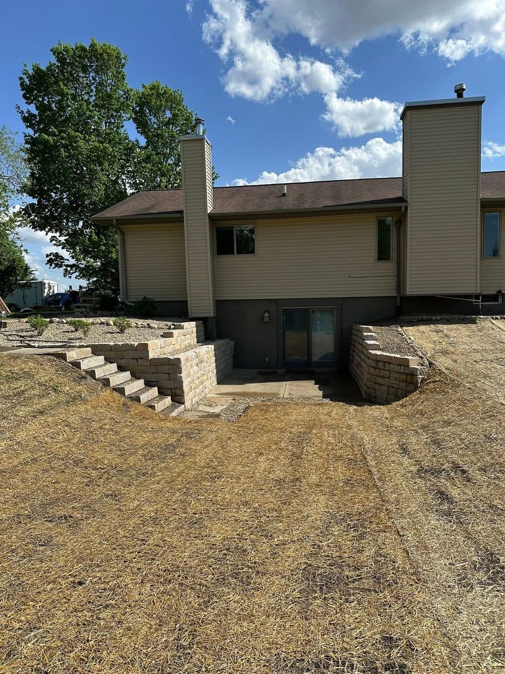 Back view of a modern home with a stone staircase leading to a landscaped yard under a blue sky.