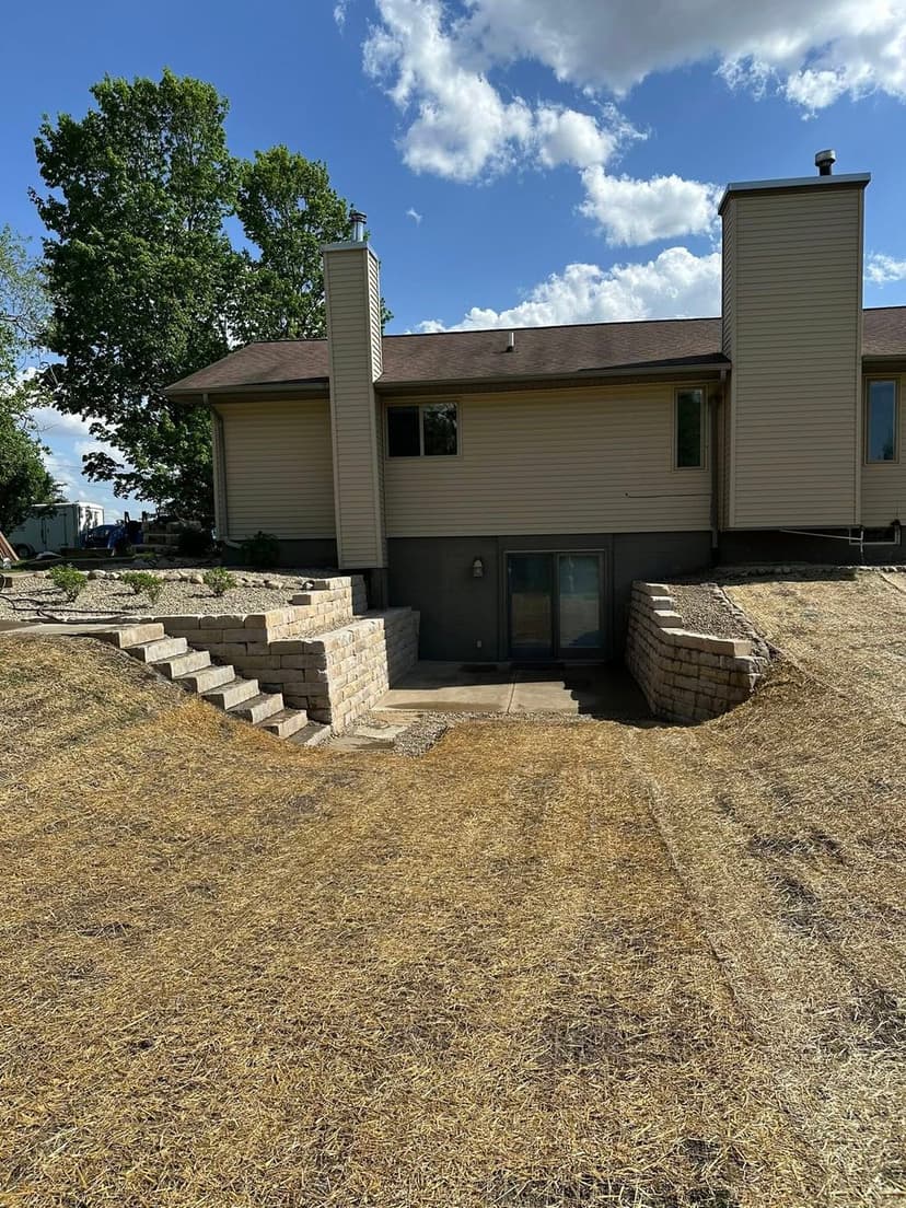 Back view of a modern home with a stone staircase leading to a landscaped yard under a blue sky.