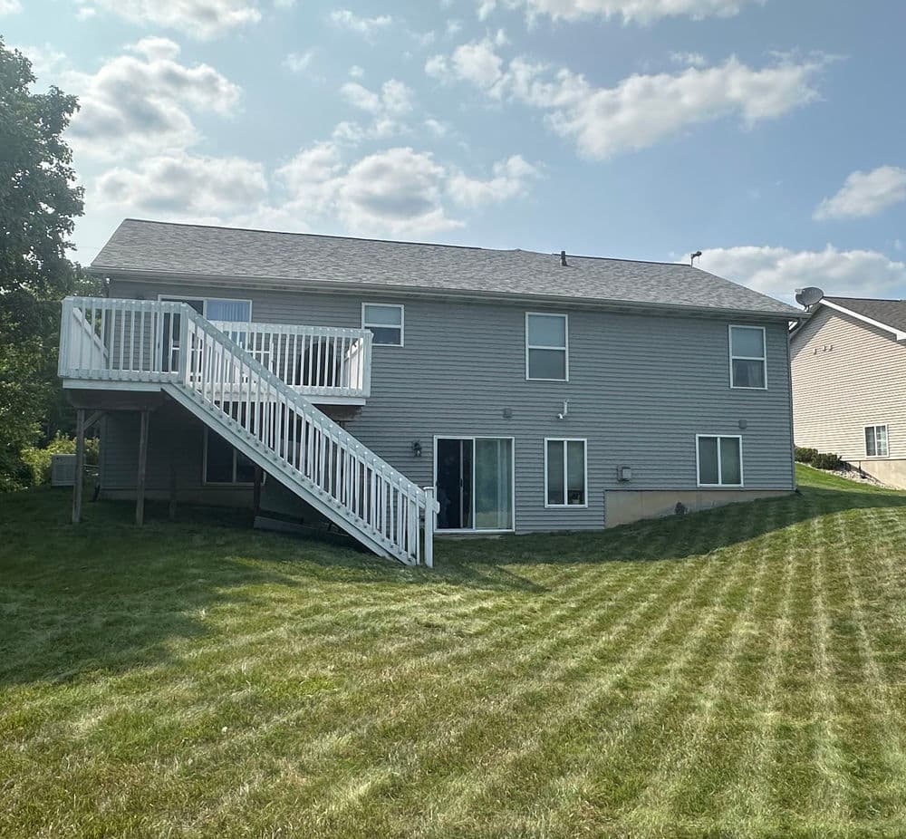 Two-story house exterior with a deck, grassy yard, and clear blue sky.