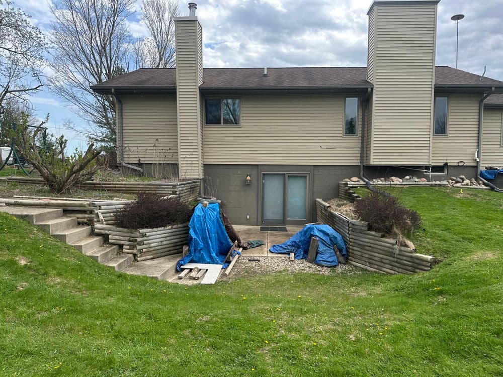 Backyard renovation with steps, stone walls, and tarps covering landscaping materials.