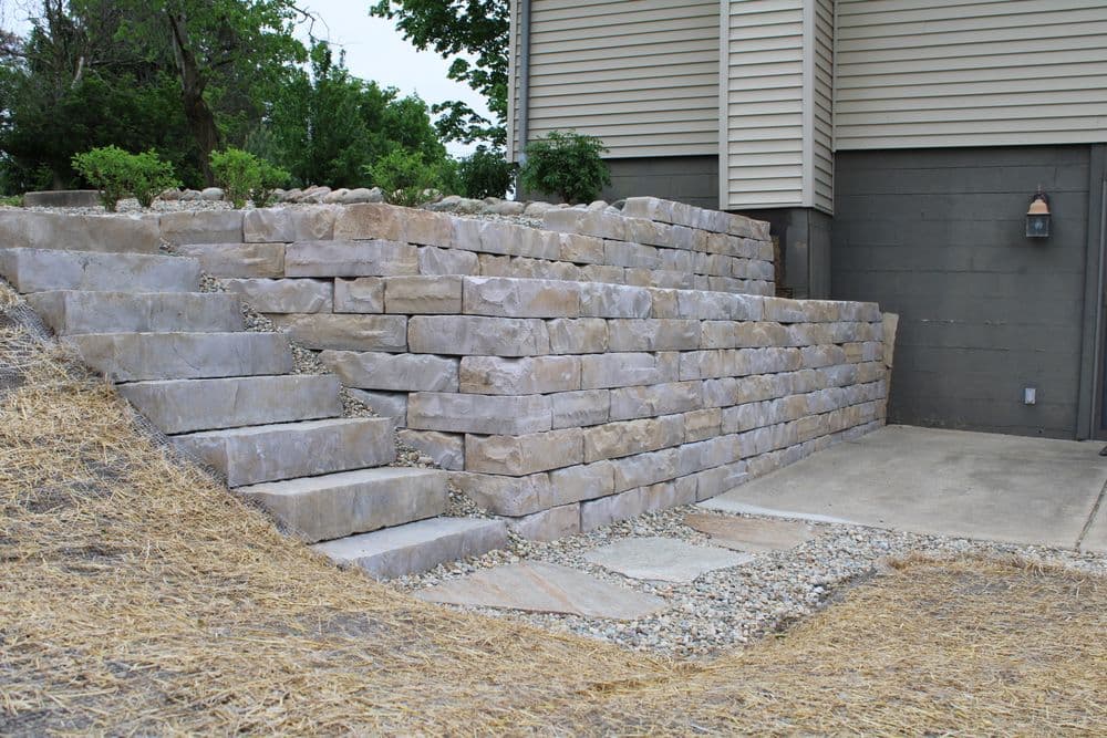 Stone retaining wall with steps leading to a home, surrounded by gravel and landscaping.