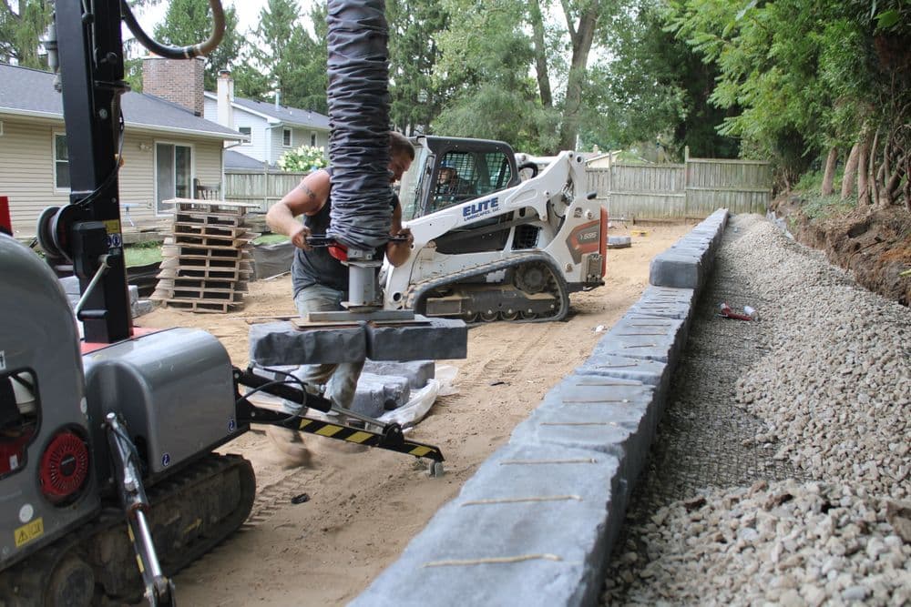 Construction worker using machinery to install a retaining wall in a backyard.