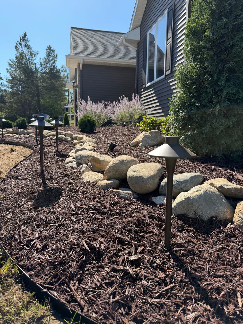 Landscaped garden with solar lights, rocks, and flowering plants by a house.