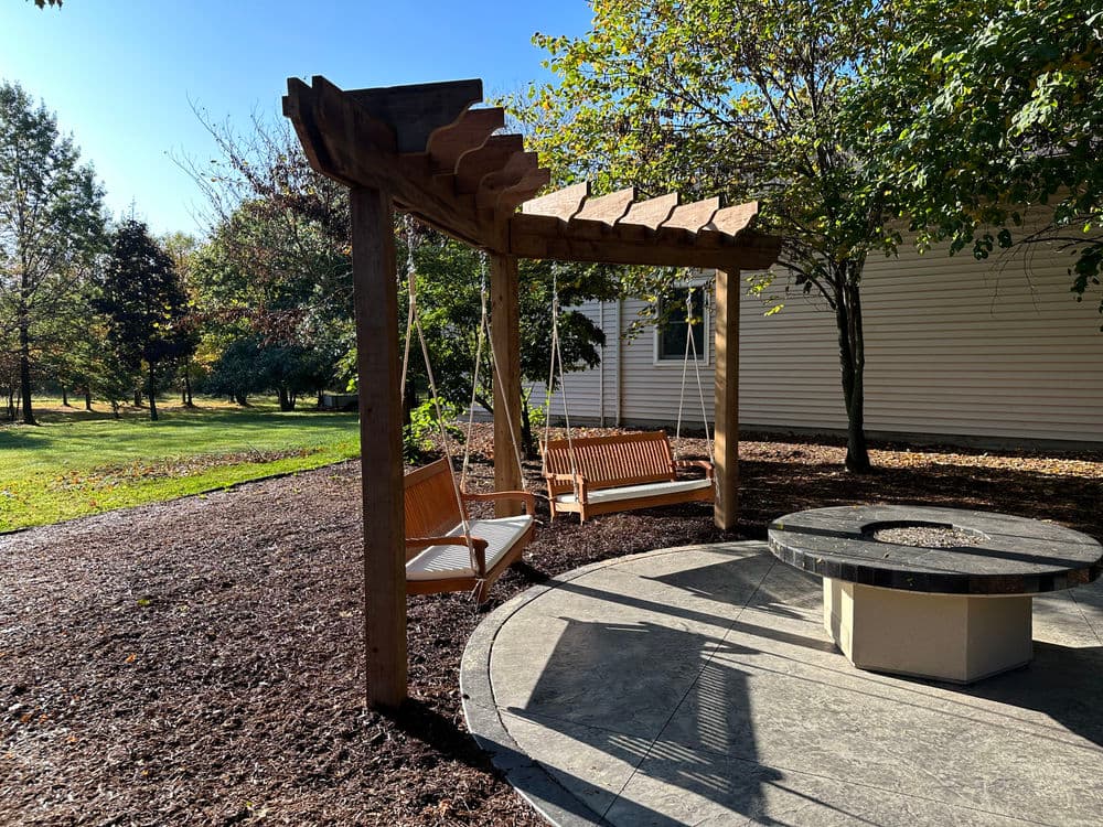 Wooden swing seating under a pergola in a sunny outdoor garden setting.