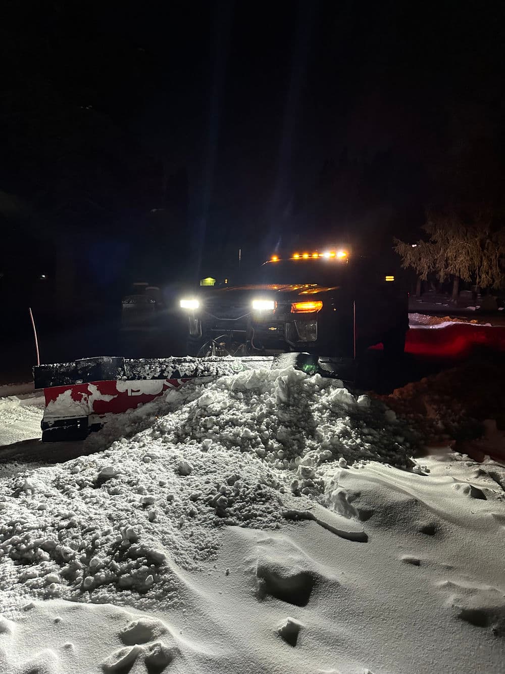 Snow plow truck illuminated at night clearing a snow-covered road.