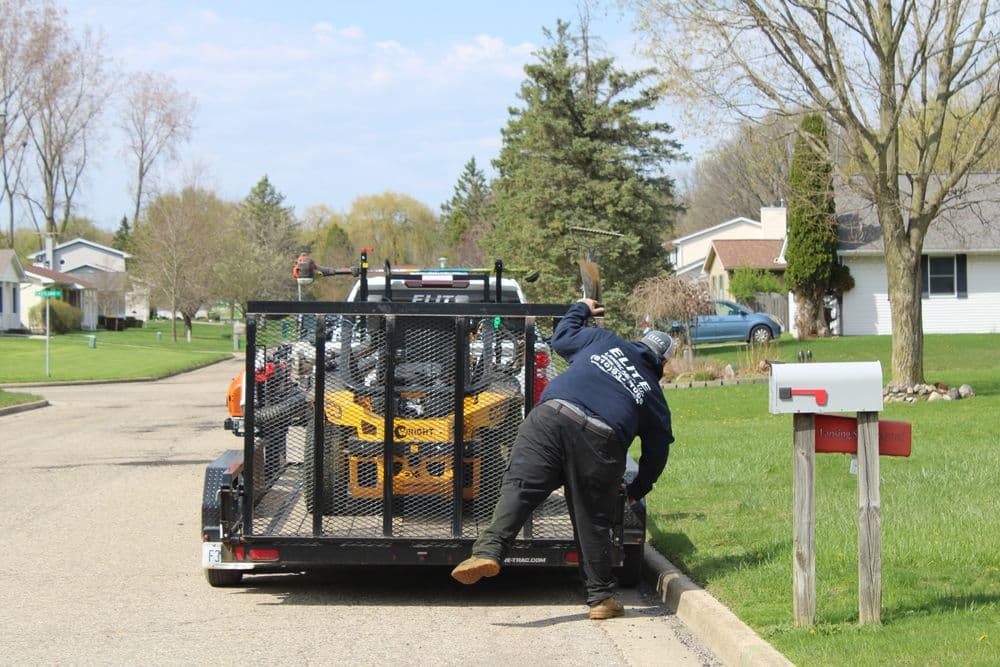 Worker unloading equipment from a trailer in a residential neighborhood on a sunny day.
